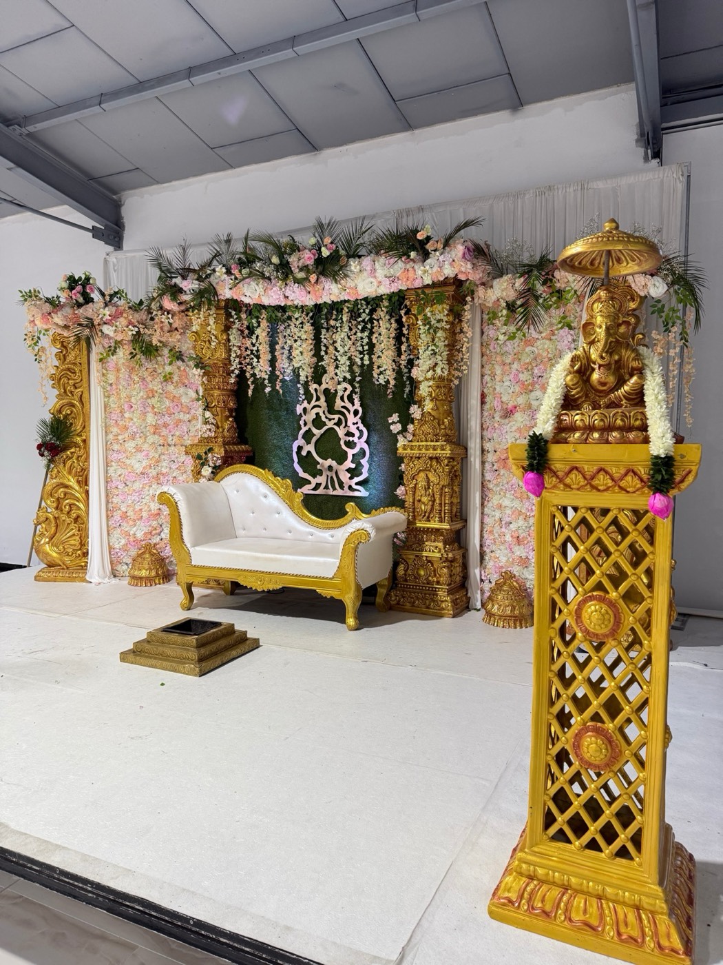 Hochzeitsbühne im Sivan-Tempel Dortmund mit weißem Sofa, Blumenwand und goldener Ganesha-Säule